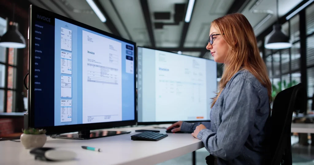 Mujer trabajando en facturación electrónica en computadora con doble monitor.