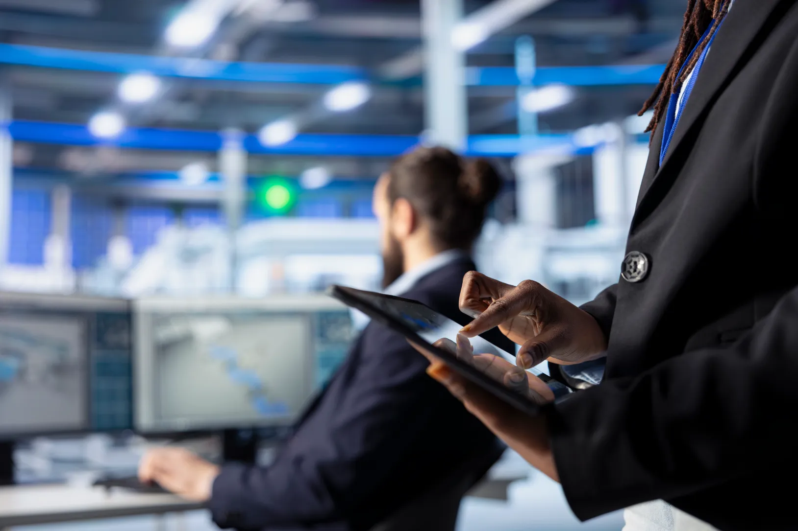 Profesional usando una tablet en una planta industrial moderna con pantallas de monitoreo al fondo.